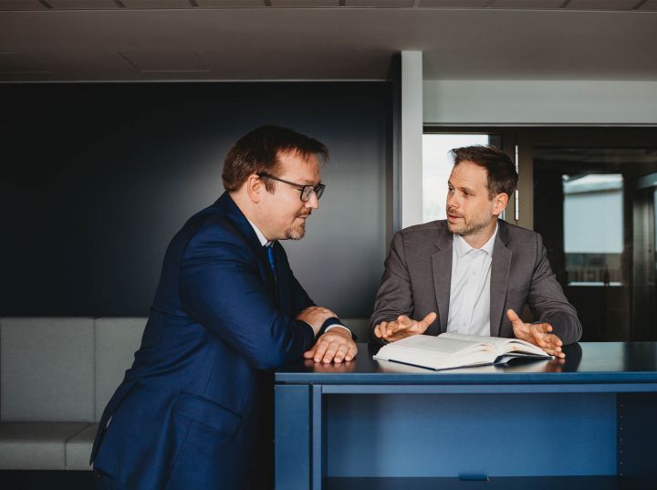 JUR URBAN - Gespräch Zwei Anwälte unterhalten sich über ein Gesetzbuch gebeugt.